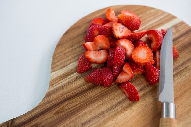 Slices of strawberries on chopping board against white background