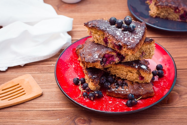 Slices of sweet black currant pie with powdered sugar on a plate on a wooden table