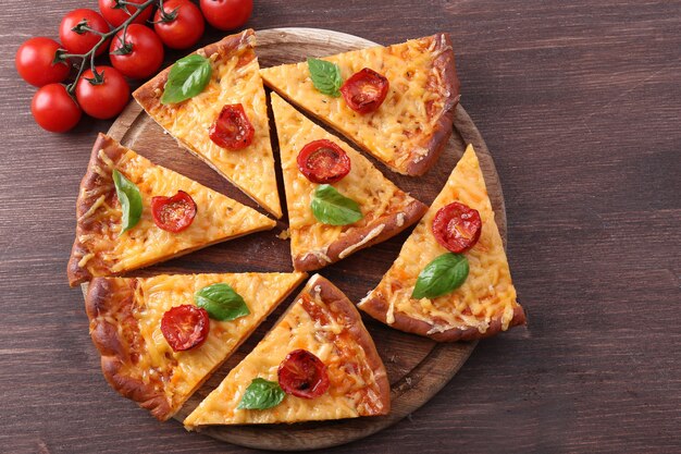 Slices of tasty cheese pizza with basil and cherry tomatoes on table close up