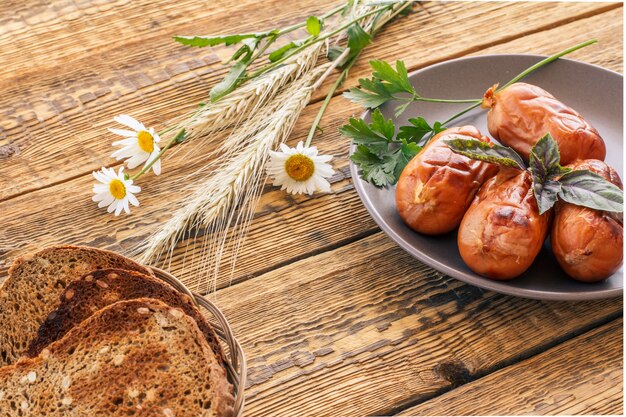 Slices of toasts in wicker basket and grilled sausages with basil and parsley on plate. Top view with wooden boards on the background..