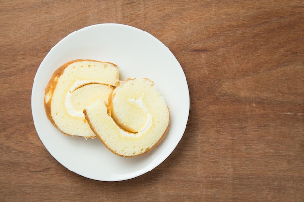 Slices of vanilla roll cake in white plate on wooden table.