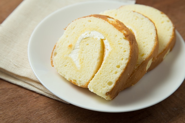 Slices of vanilla roll cake in white plate on wooden table.