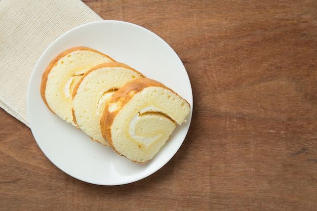 Slices of vanilla roll cake in white plate on wooden table.