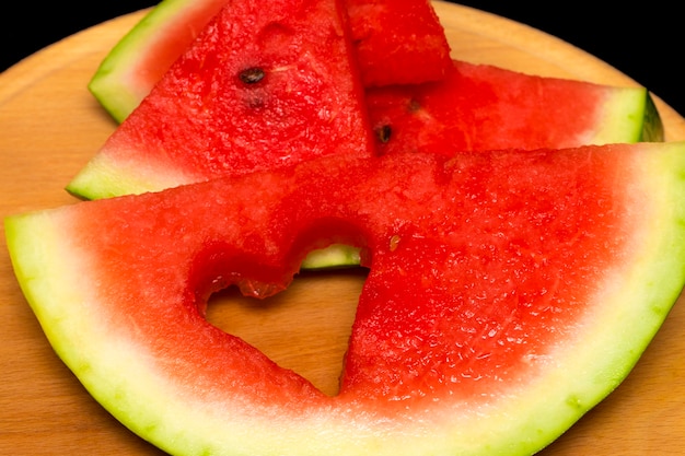 Slices of watermelon, heart on wooden background.