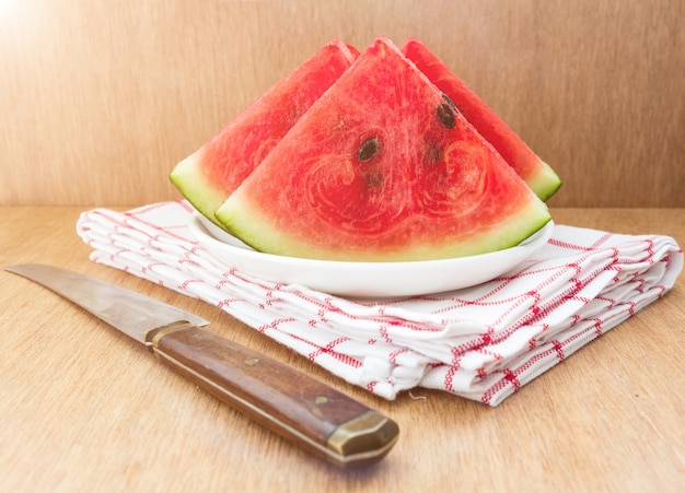 Slices of watermelon and a knife on a plate on a wooden background