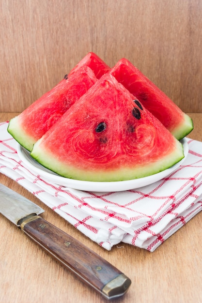 Slices of watermelon and a knife on a plate on a wooden background
