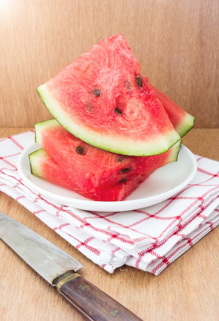 Slices of watermelon and a knife on a plate on a wooden background