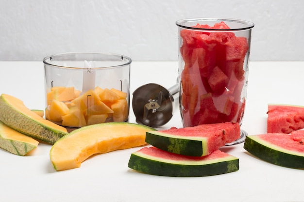 Slices of watermelon and melon. Pieces of melon and watermelon in blender jar. Metal blender. White background.