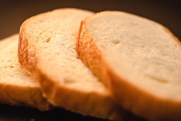 Slices of white bread close up on a black background rough dappled textured surface chopped pieces loaf of natural organic food with holes