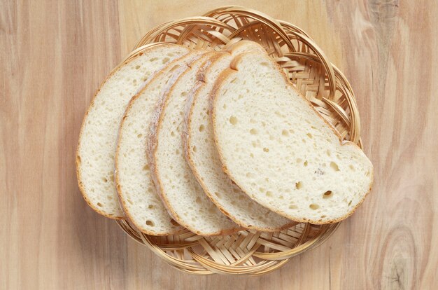 Photo slices white bread in wicker plate on wooden table