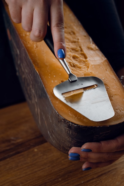 Photo slicing aged cheese parmesan with crystals using a slicer knife. hard cheese with knife for appetizer