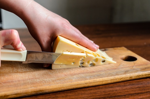 Нарезка сыра на деревянной доске.