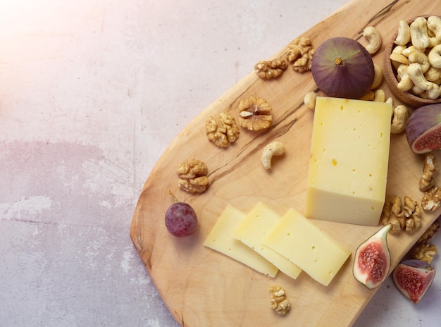 Slicing cheese with fruits - nuts and figs on a wooden board. Delicious snack