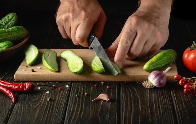 レストランやホテルの野菜サラダや食事メニューを準備するために、シェフの手でまな板の上できゅうりをスライスする