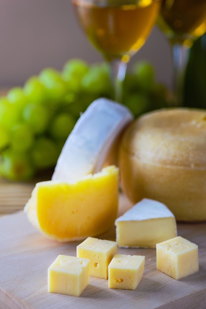 Slicing of different types of cheeses on grapes and glasses with white wine.