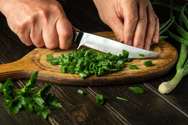 Affettare le cipolle verdi su un tagliere con un coltello per cucinare cibo vegetariano