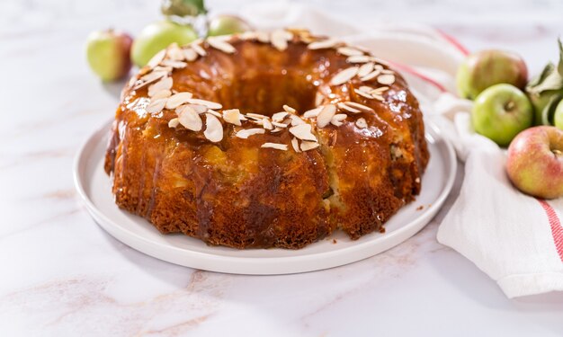 Slicing homemade apple bundt cake and garnishing with sliced almonds.