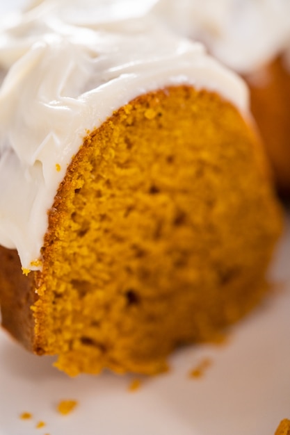 Slicing homemade pumpkin bunt cake with cream cheese frosting.