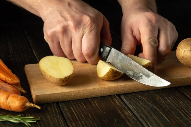 사진 요리사의 손에 칼을 들고 주방 절단판에 생 감자를 잘라 집에서 채소 요리를 요리하는 것