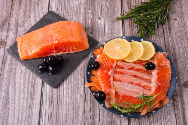 Slicing red fish on a plate with olives lemon and rosemary