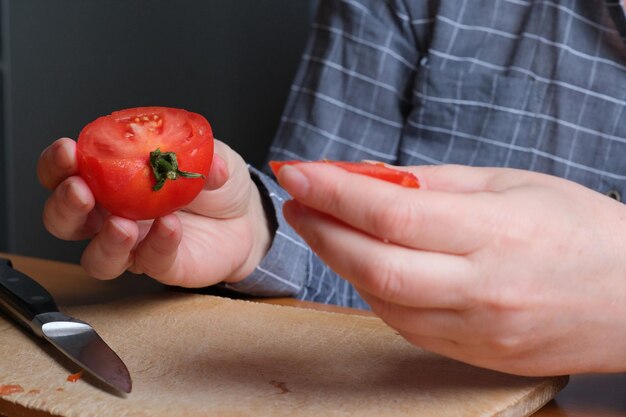 Slicing a red ripe tomato An elderly woman's hands hold a tomato for slicing on a table in the kitchen Closeup plan
