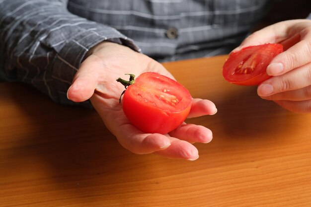빨갛게 익은 토마토를 썰다 한 나이든 여성의 손이 부엌 테이블 위에 썰기 위해 토마토를 들고 있다