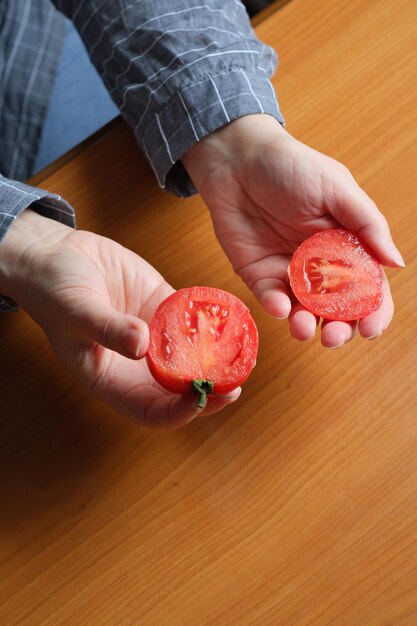 빨갛게 익은 토마토를 썰다 한 나이든 여성의 손이 부엌 테이블 위에 썰기 위해 토마토를 들고 있다