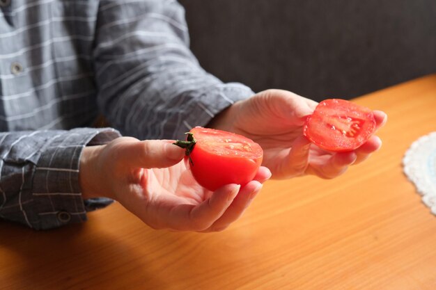 Slicing a red ripe tomato an elderly woman's hands hold a tomato for slicing on a table in the kitchen closeup plan