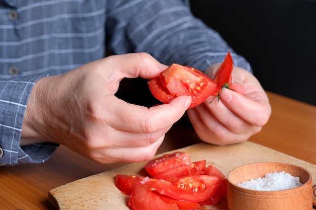 Photo slicing a red ripe tomato an elderly woman's hands hold a tomato for slicing on a table in the kitchen closeup plan