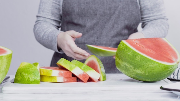 Slicing red watermelon into small pieces on a white cutting board.