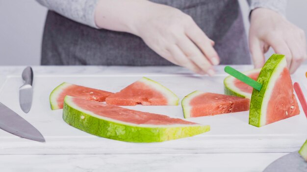 Slicing red watermelon into small pieces on a white cutting board.