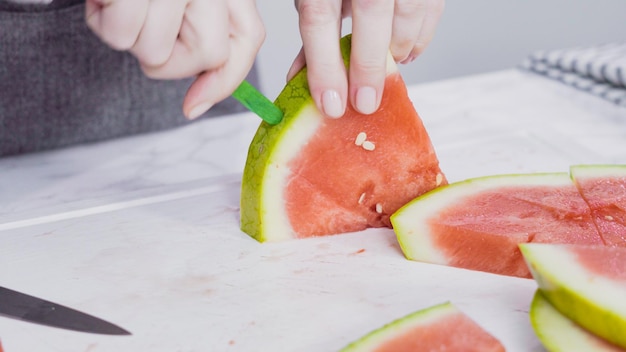 Slicing red watermelon into small pieces on a white cutting board.