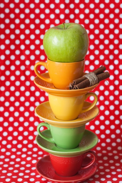 Slide of multicolored cups and green apple stand on a red polka dot background