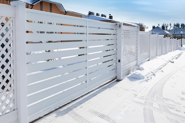 Sliding plastic gates for the entrance of a car in a suburban village. Car tracks on a snowy road