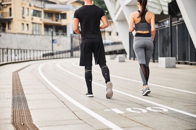 Slim athletic man and woman in sportwear are spending time actively going jogging in city centre