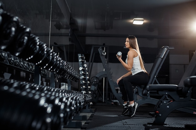 Slim, bodybuilder girl, lifts heavy dumbbell standing in front of the mirror while training in the gym. Sports concept, fat burning and a healthy lifestyle. High quality photo