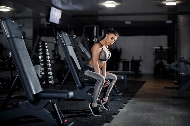 Slim, bodybuilder girl, lifts heavy dumbbell standing in front of the mirror while training in the gym. Sports concept, fat burning and a healthy lifestyle. High quality photo