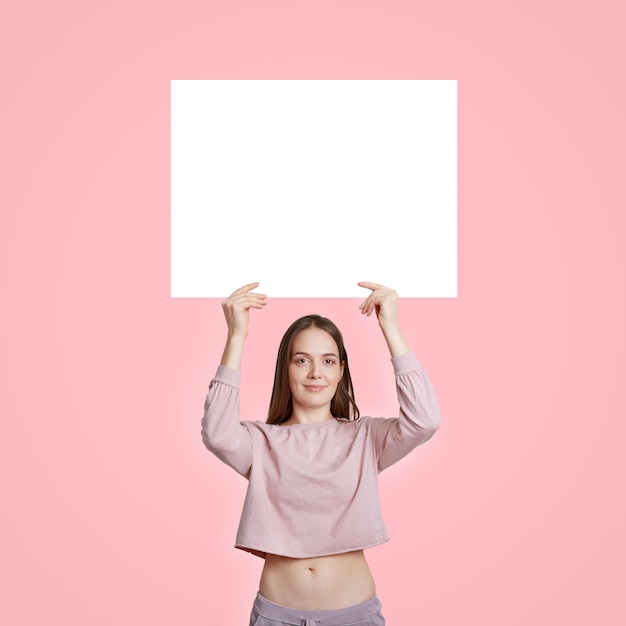 캐주얼 옷에 슬림 백인 여자 광고 또는 홍보 내용, 핑크에 고립 된 흰색 빈 흰색 카드를 보유하고있다. 자유 공간. 세로 샷.