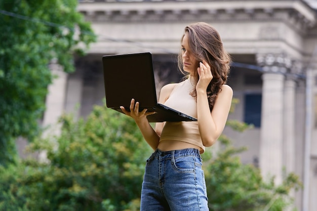 Slim caucasian woman with notebook stands in garden at daytime