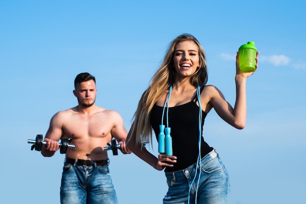 Slim female trainer of fitness with protein shaker man and girl with protein shake bottle and skippi...