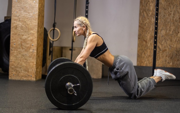 Photo slim fit woman with long pigtails trains the abdominal muscles rolls the barbell on the floor in a modern functional gym perfect body and trained muscles concept