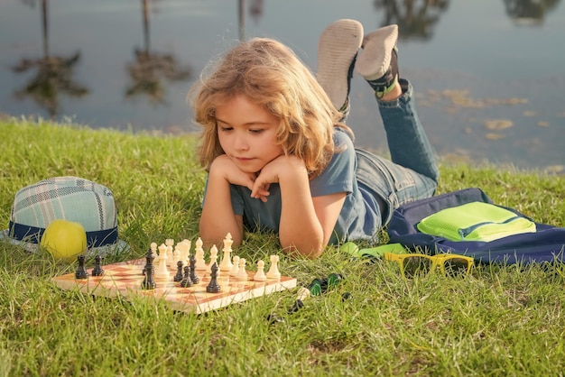 Slim geconcentreerd en denkend kind dat buiten in het park schaakt