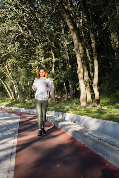 Slim ginger woman in sport clothes running in park on morning. Healthy fitness lifestyle.