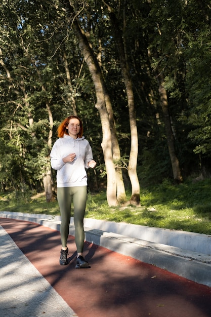 Slim ginger woman in sport clothes running in park on morning. Healthy fitness lifestyle.