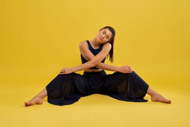 Slim girl doing stretching with legs wide apart and cross arms in studio