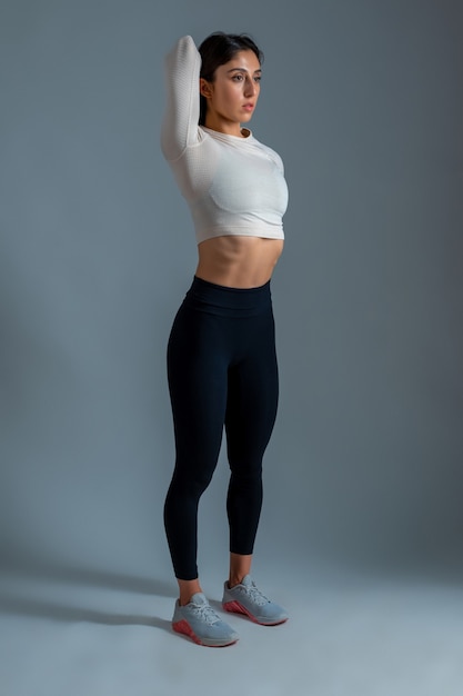 Slim girl doing stretching workout on grey wall