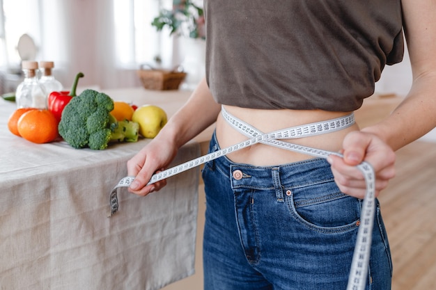Slim girl measures the waist in the kitchen