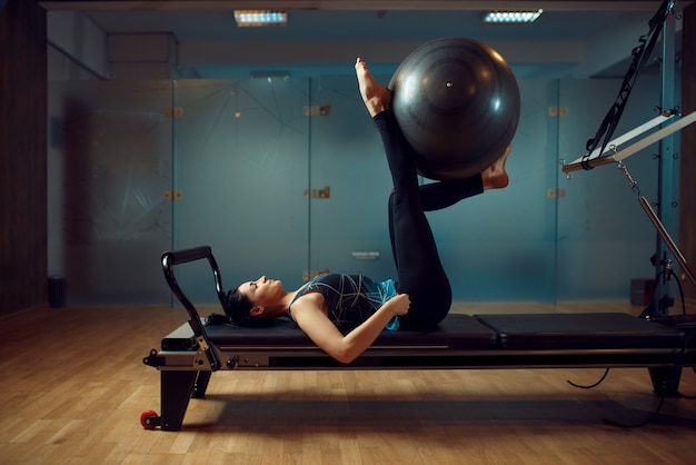 Slim girl in sportswear, pilates training with ball on exercise machine in gym. Fitness workuot in sport club.