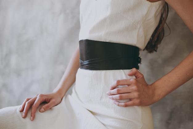 A slim girl in a white dress tries on a belt with black leather