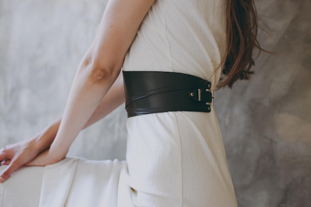 A slim girl in a white dress tries on a belt with black leather